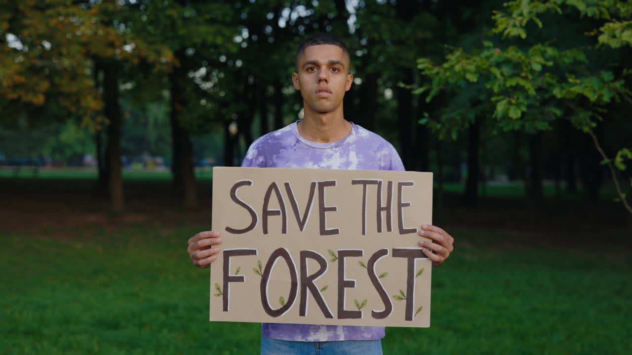 Man holding "Save the Forest" protest sign in park