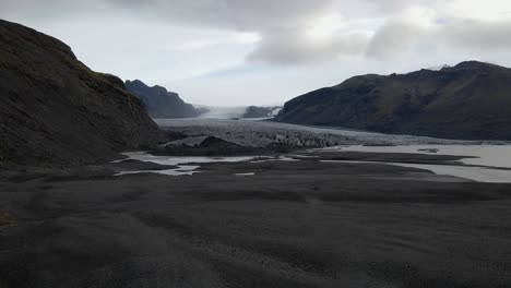 Establishing-shot-of-Skaftafell-Glacier-surrounded-by-mountains,-Drone-flying-towards-Glacier-tongue,-Iceland