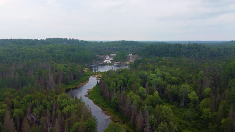 Aerial-drone-shot-tracking-up-a-river-to-a-fast-flowing-waterfall-cascading-over-a-rocky-outcrop-in-Massey,-Ontario,-Canada