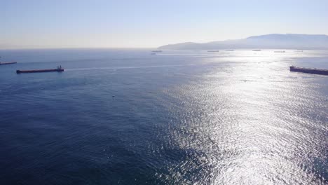 large bulk carrier passes another freighter in the strait of gibraltar as several ships are anchored for algeciras and a ferry in the background is moving at high speed to africa