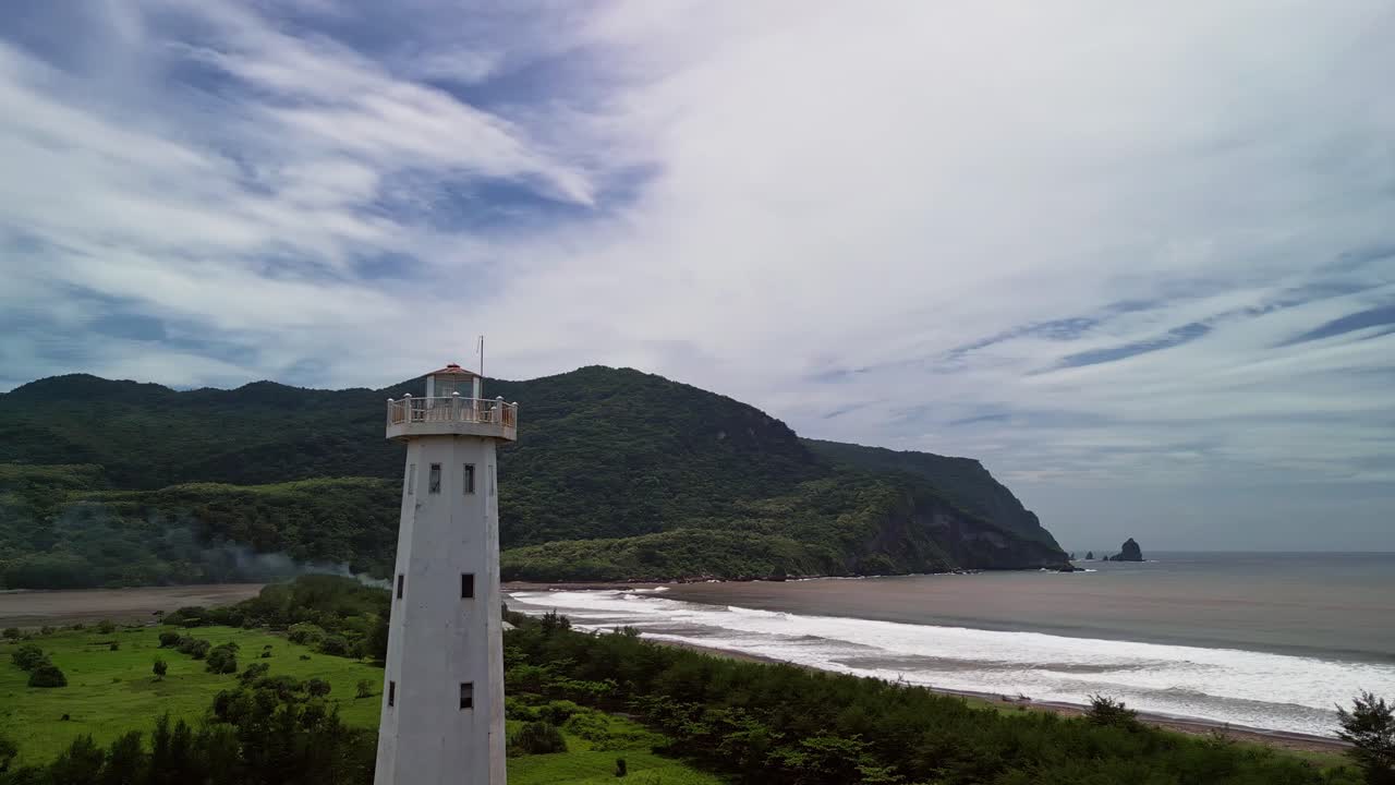 Cinematic drone footage capturing a lighthouse on the coastline with natural hills, open ocean views and soft waves creating a relaxed marine atmosphere