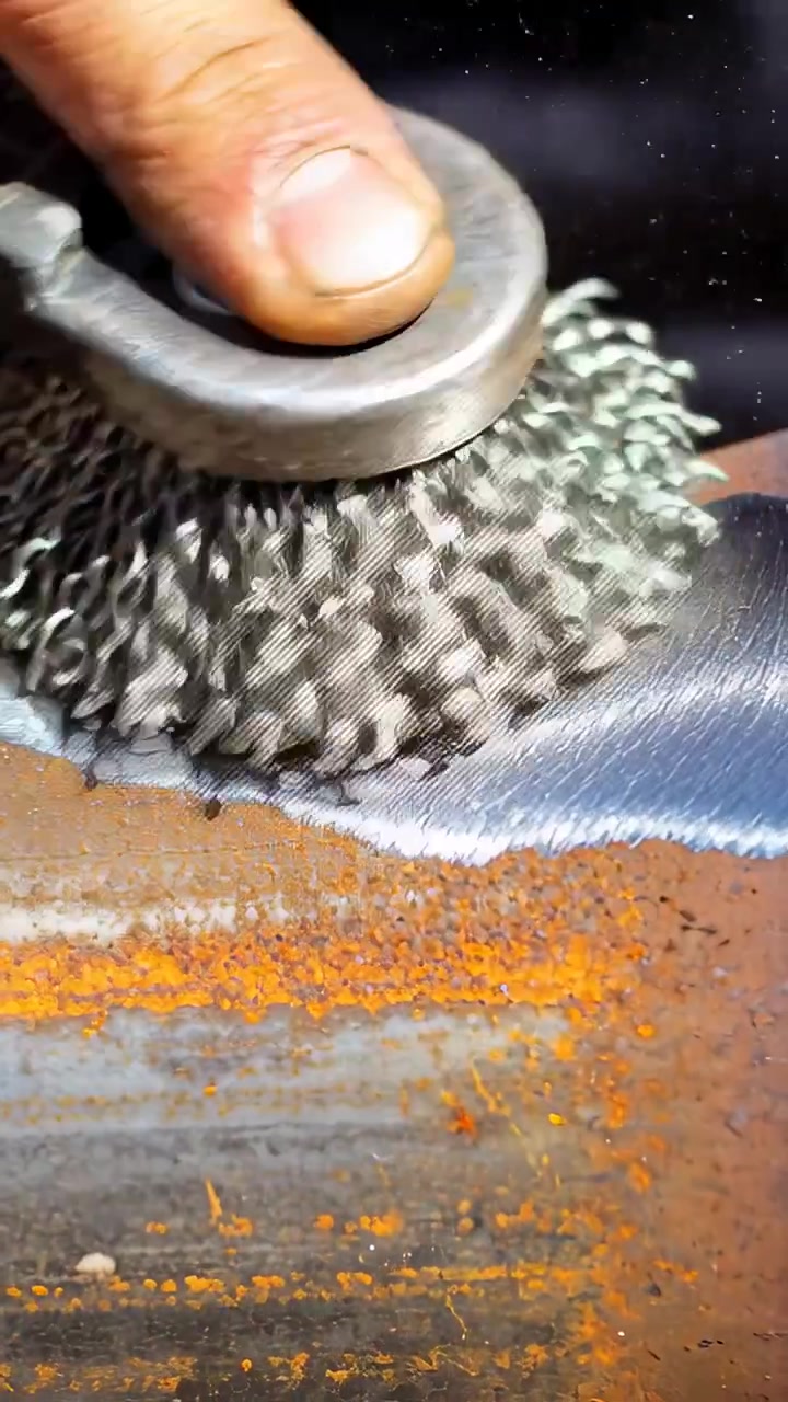 Video vertical: Colocando un cepillo de copa de alambre, lijando a mano acero oxidado en un garaje, preparando para soldar.