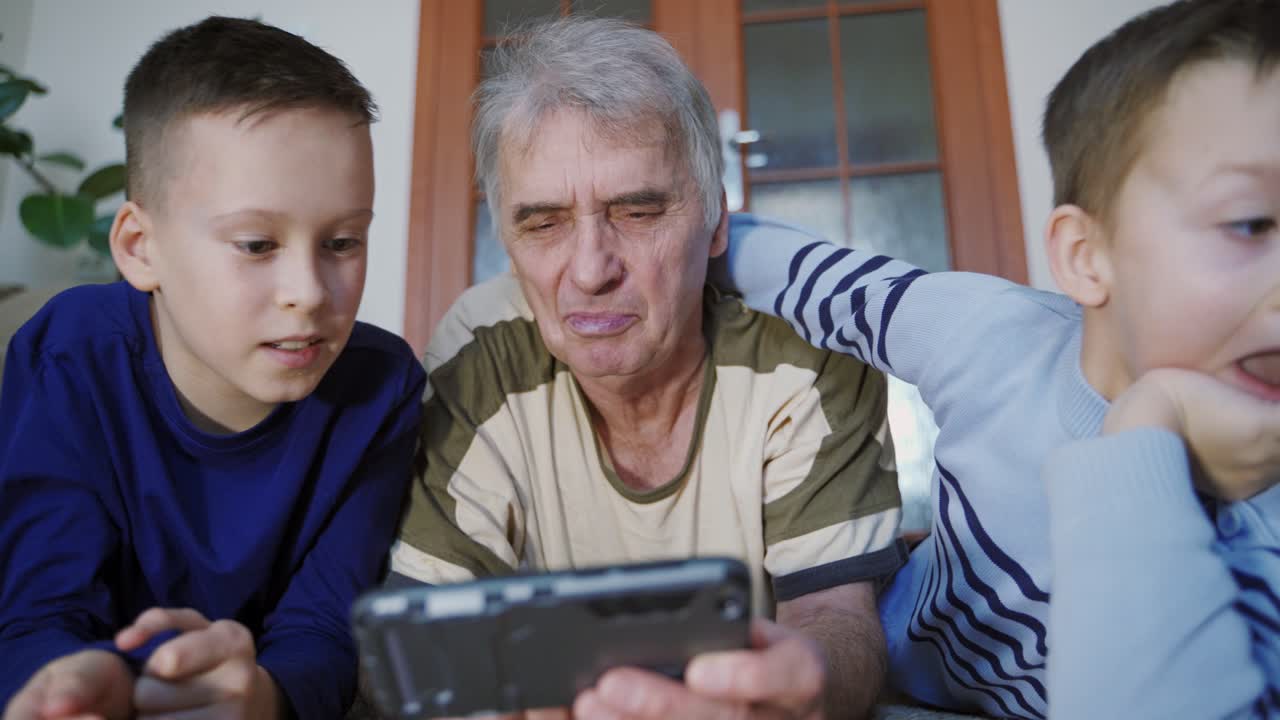 Senior grandfather and a small grandchildren playing game on smartphone at home. Family idyll.