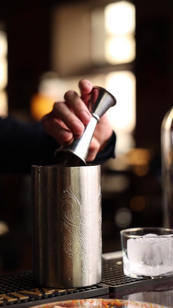 Barman che versa alcol in uno shaker da cocktail di metallo