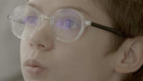 Closeup-of-a-young-boy-wearing-glasses-and-staring-up-at-a-screen-playing-video-games