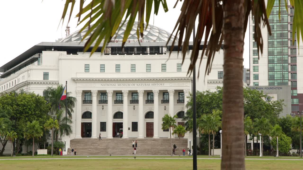 Inquadratura ampia e statica dell'edificio bianco del museo neoclassico dietro le palme a Manila.