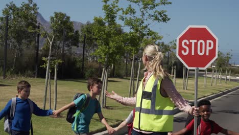 mujer con chaleco alto sosteniendo una señal de parada mientras un grupo de niños cruzan la carretera