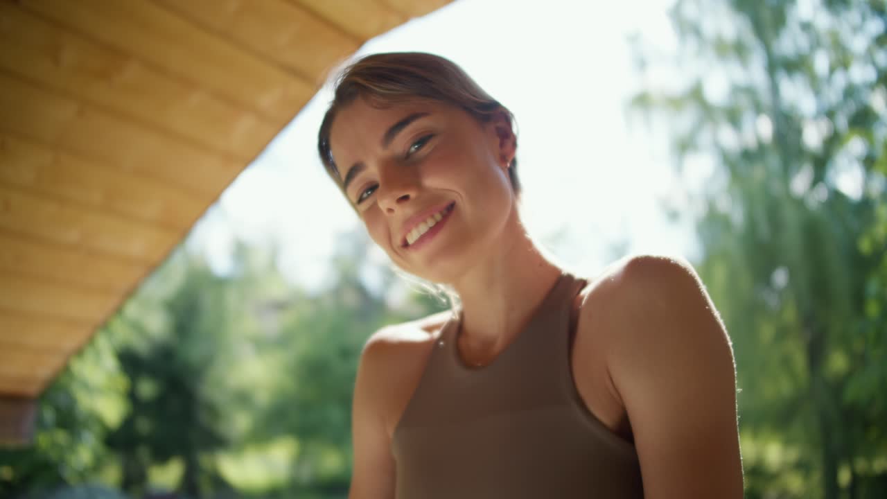 Portrait of a beautiful blonde girl in a light brown T-shirt who smiles and looks at the camera against the backdrop of nature in the gazebo