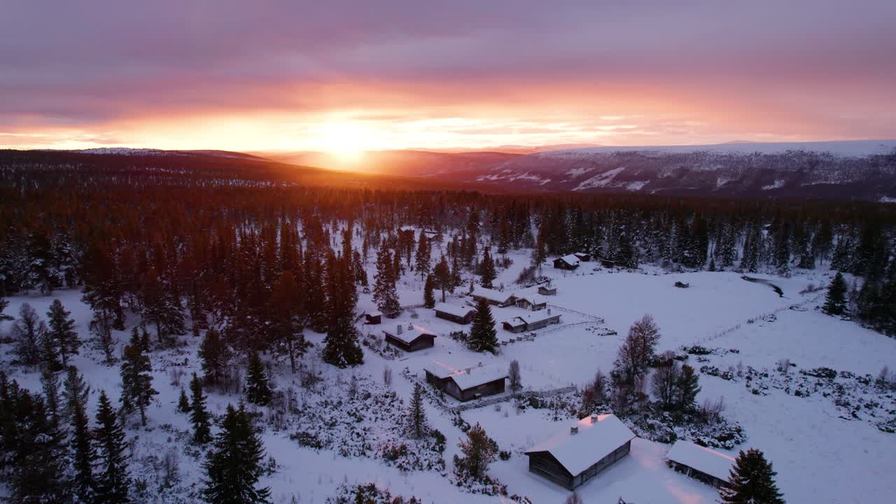 Hehkuva auringonlasku talvisen vuoristometsämaiseman yllä, jossa on puumökkejä.