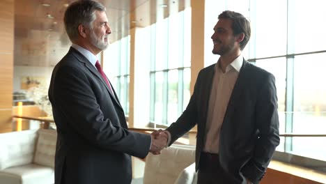 confident caucasian mature businessman handshaking male partner at office meeting. partnership, investment concept