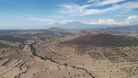 Vista-Aérea-De-Las-Tierras-De-Cultivo-En-El-Estado-Mexicano-De-Tlaxcala,-Con-Los-Volcanes-O-Montañas-Iztaccíhuatl-Y-Popocatepetl-Al-Fondo