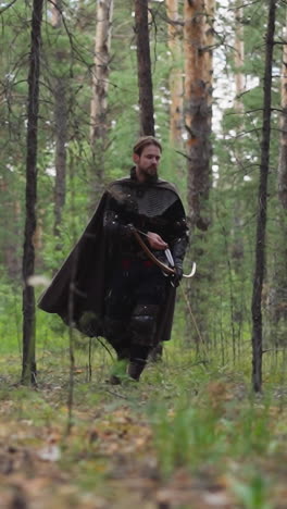 explorador medieval con un arco grande busca huellas de enemigos en el bosque a cámara lenta. viejo soldado en cadena de correo camina a través del bosque. recreación histórica