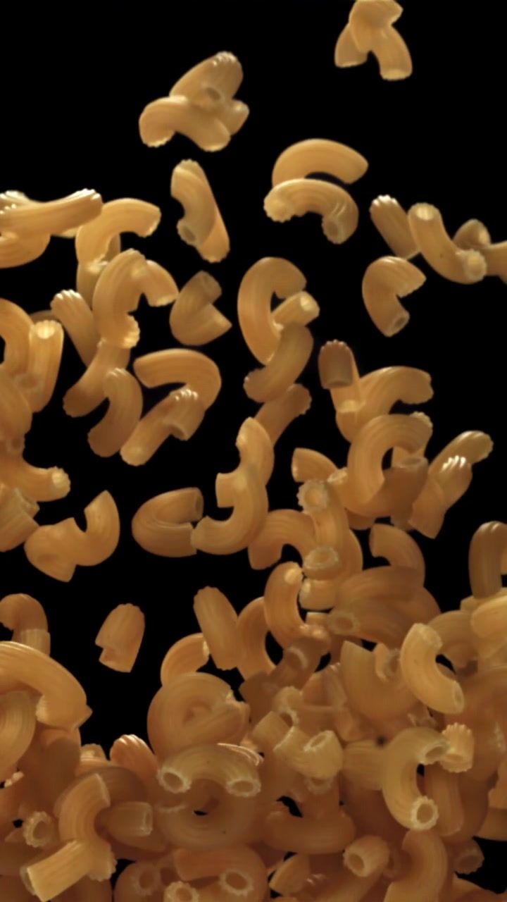 Pasta maccheroni secca che cade al rallentatore su sfondo nero.