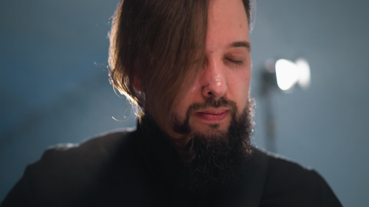 vista en primer plano de la cara de un hombre barbudo con luz de fondo, con una camisa negra contra un fondo borroso