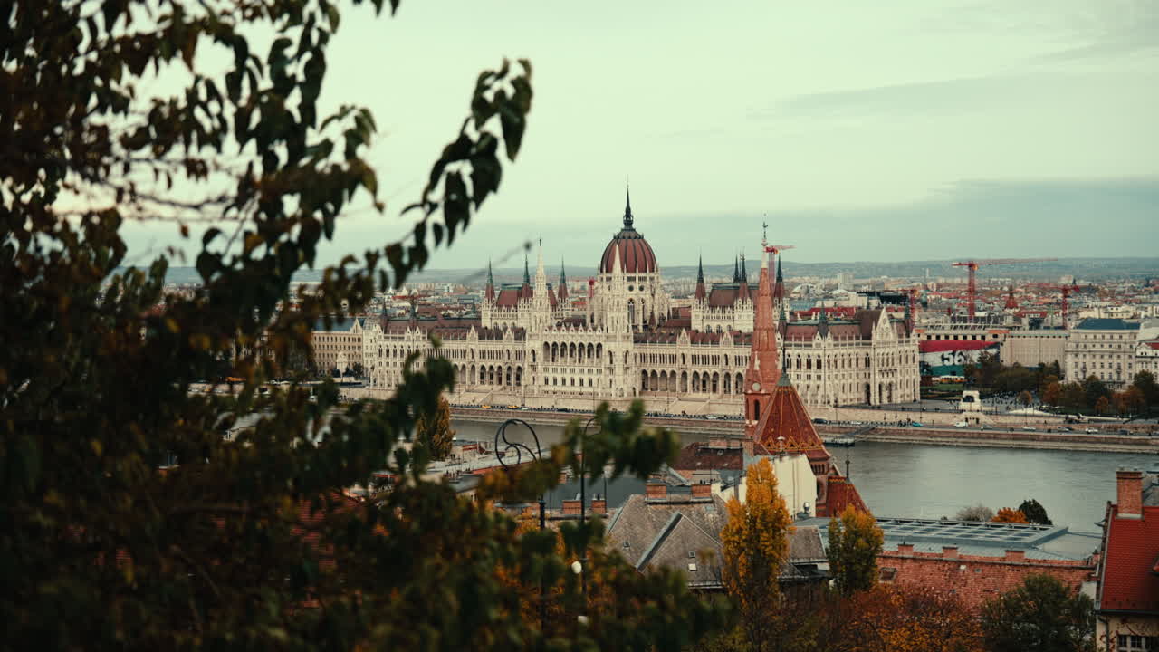 Panoramic view of Budapest featuring the iconic Parliament building along the Danube River on a cloudy day. Capture the historic city center, bridges, and urban landscape from afar