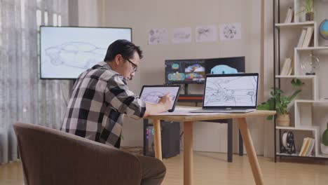 side view of asian male celebrating success drawing new car design concept on a tablet in the studio with tv and computers display 3d electric car model