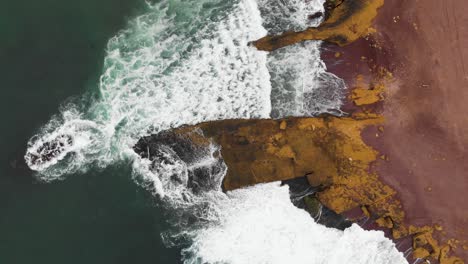 Ascending-aerial-shot-of-waves-crushing-in-to-a-huge-cliff-at-the-ocean-coastline