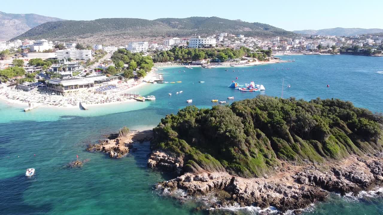 크사밀 해변, 이오니아 해, 알바니아 - 섬, 선베드, 보트, 호텔, 리조트, 산, 수상 놀이터의 공중 드론 보기
