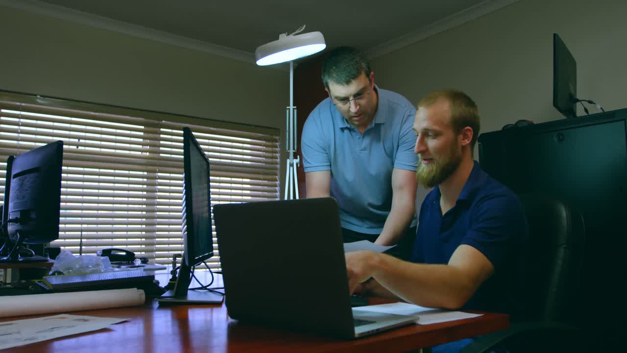 Male robotic engineers discussing over laptop at desk 4k