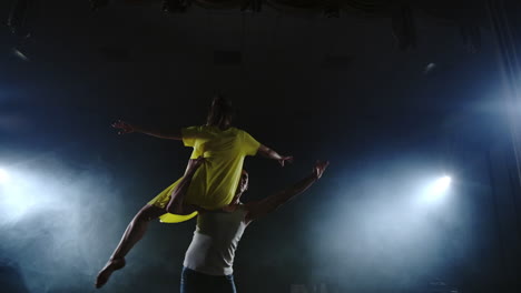 Zoom-camera-two-modern-ballet-dancers-are-dancing-on-stage-in-smoke-a-man-raises-his-partner-in-his-arms-and-rotates-in-the-air.-The-musical-uses-circus-acrobats-dancers.