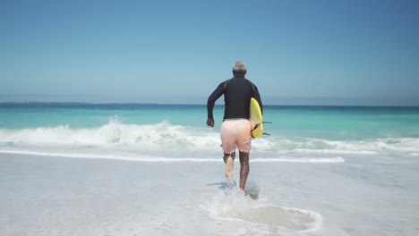 Senior man running to the ocean with a surfboard