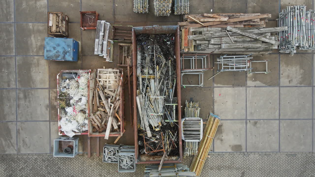 Top down aerial of metal waste material lying in a large container for recycling. The drone descends to the sorted metal