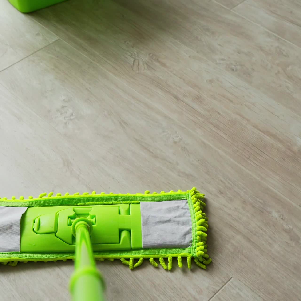 Green mop and bucket on wooden floor at home. Housewife cleaning the parquet floor with a modern microfiber brush. Daily routine.