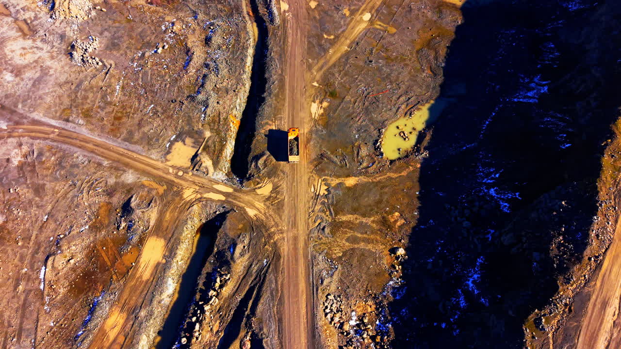 Heavy hauler truck transporting materials along a dusty path in a stone quarry. Orange dump truck driving on dirt road in mine