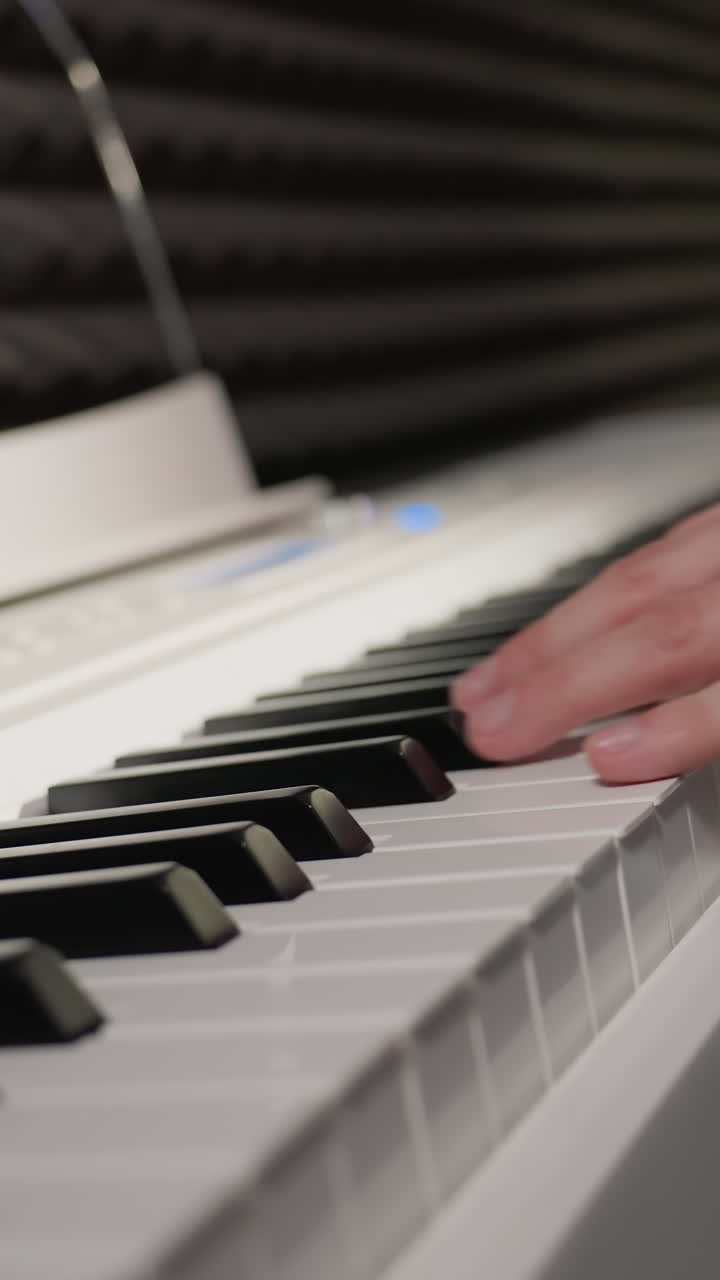 primer plano de una mano con una camisa de manga larga azul tocando un piano blanco, con el fondo mostrando una pared acústica negra y un toque de vaqueros de denim. enfoque en las teclas del piano y la mano del músico
