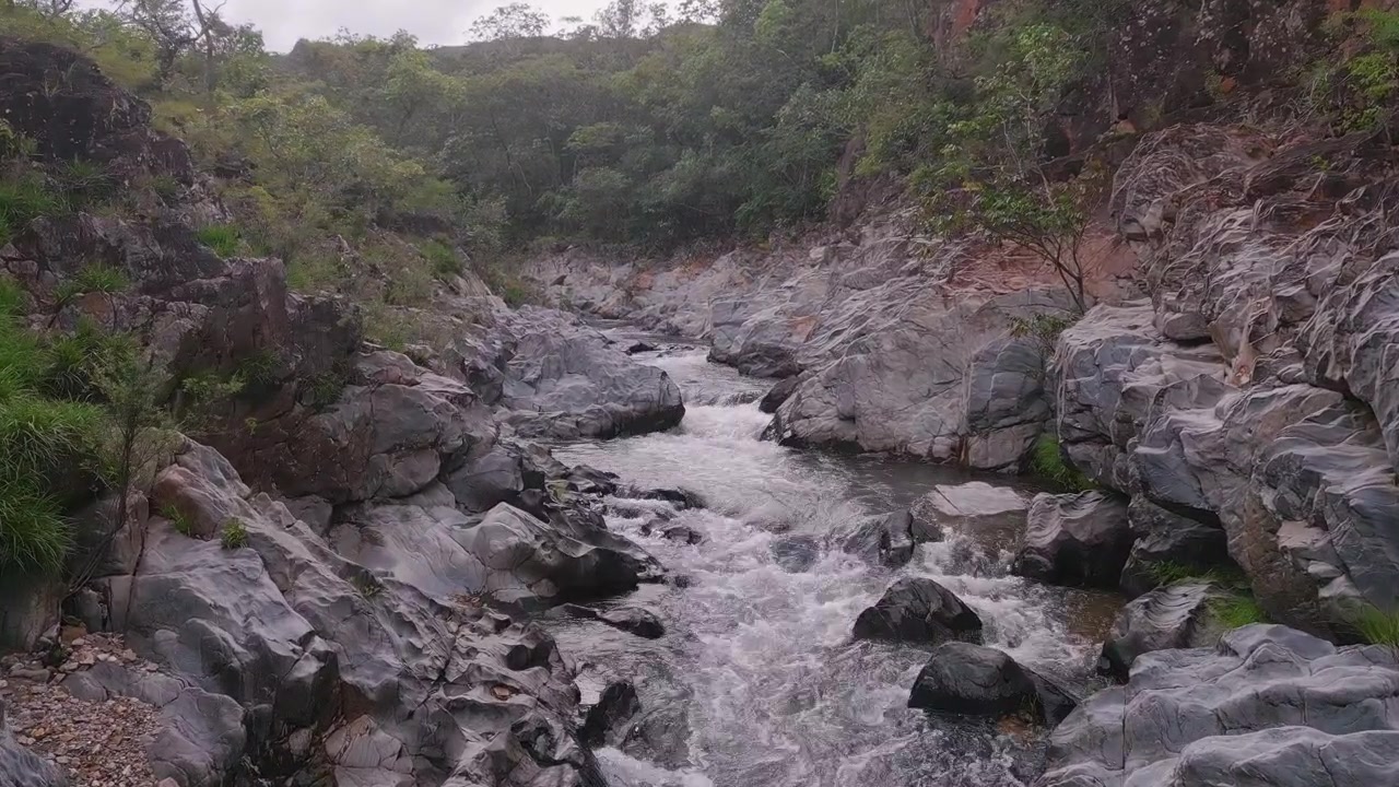 Fiume São Miguel che scorre attraverso un aspro canyon di quarzite nella Serra do Segredo, Chapada dos Veadeiros, Goiás, Brasile, circondato da vegetazione preservata del Cerrado, sorvolo basso in avanti con drone sopra le rapide.