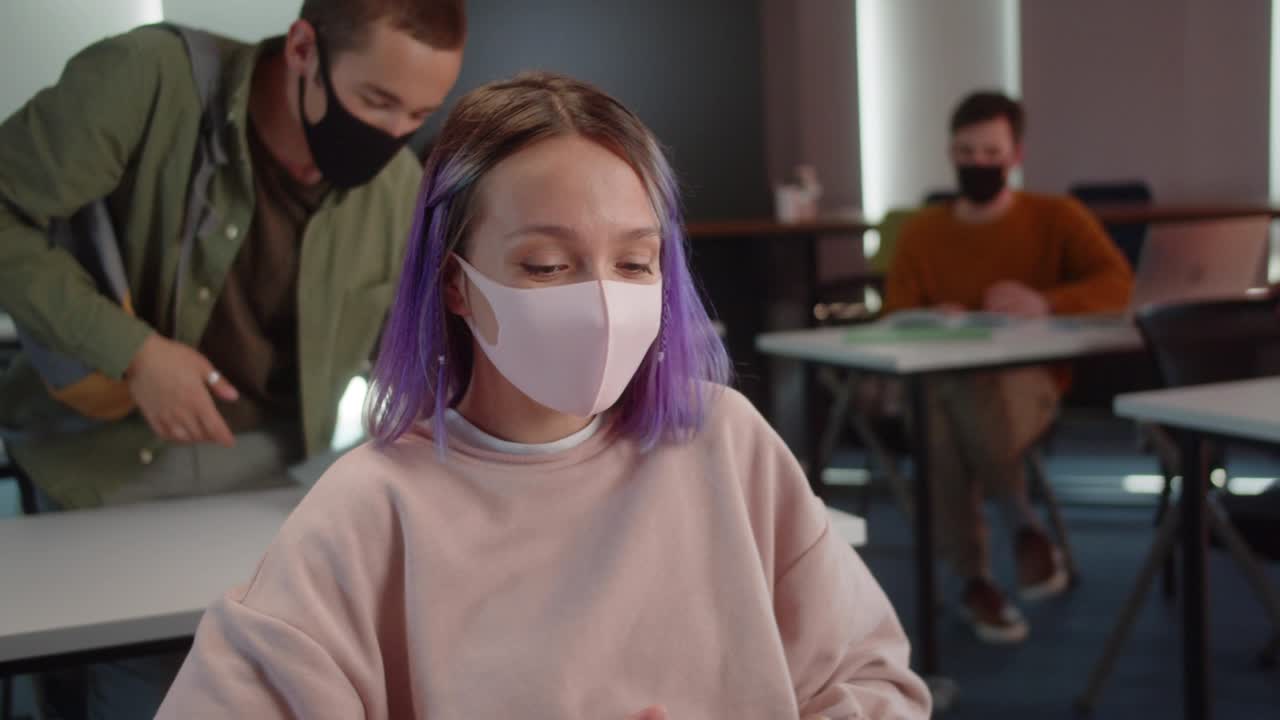 un atractivo estudiante está entrando en el aula, saludando a sus compañeros de clase y sentándose en su escritorio