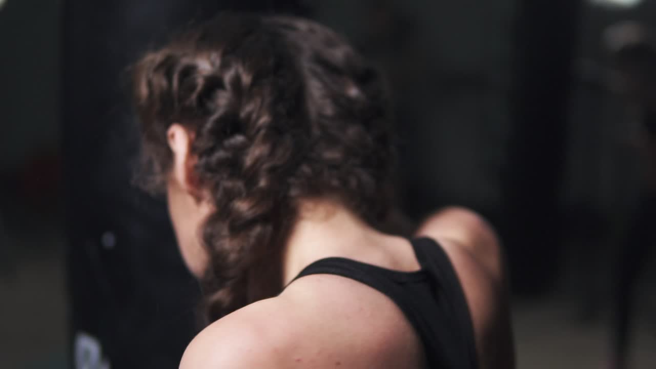 mujer joven entrenando con un saco de boxeo en un club de boxeo. vista posterior de una mujer joven entrenando con las manos envueltas en boxeo