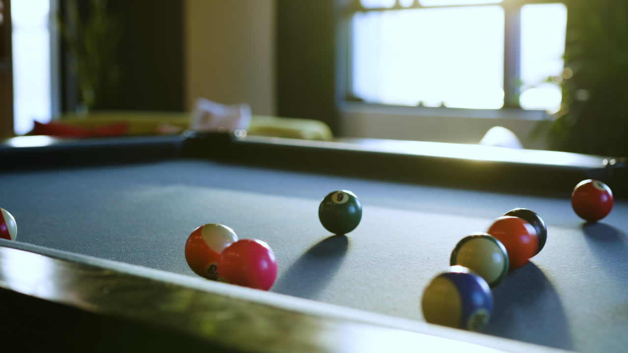 Des boules de billard de différentes couleurs reposent sur une table de billard sombre, prêtes pour une partie. Des amis se rassemblent, profitant d'une soirée de compétition amicale et de rires.
