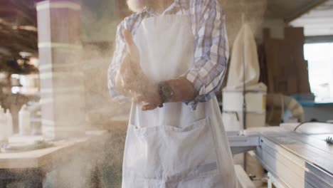 african american male carpenter wearing an apron dusting his hands at a carpentry shop