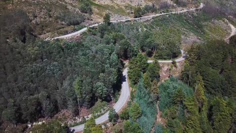 Small-white-caravan-going-up-a-road-on-the-side-of-the-mountains-in-Portugal-,-shot-on-drone