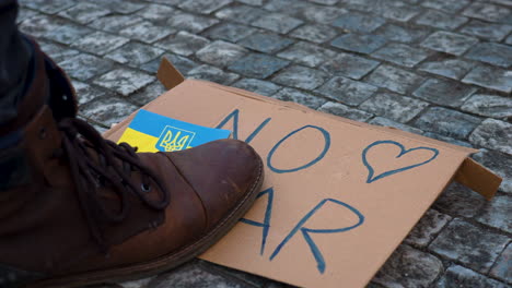 boot stepping on cardboard sign against war in ukraine on cobblestones