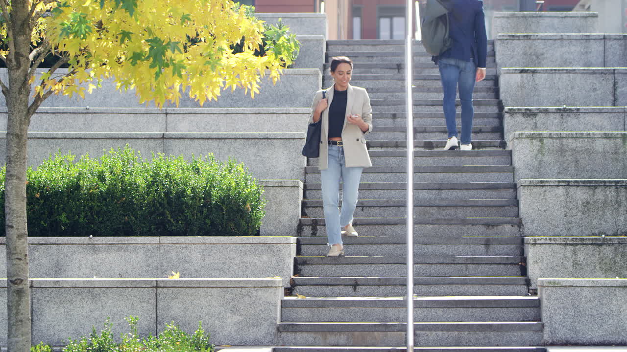 Forretningsmand og forretningskvinde pendler udendørs og passerer hinanden på trapperne på vej til arbejde