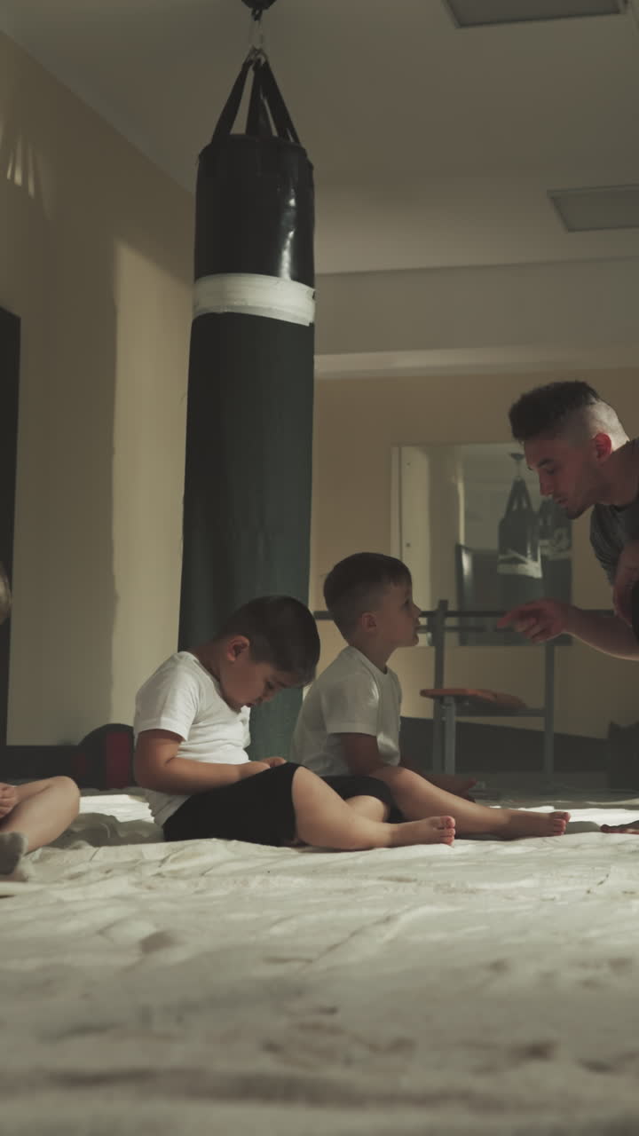 el instructor regaña a los niños traviesos en el club de boxeo. los niños cansados se sientan en el suelo escuchando al instructor de combate en el gimnasio en cámara lenta. clase de artes marciales