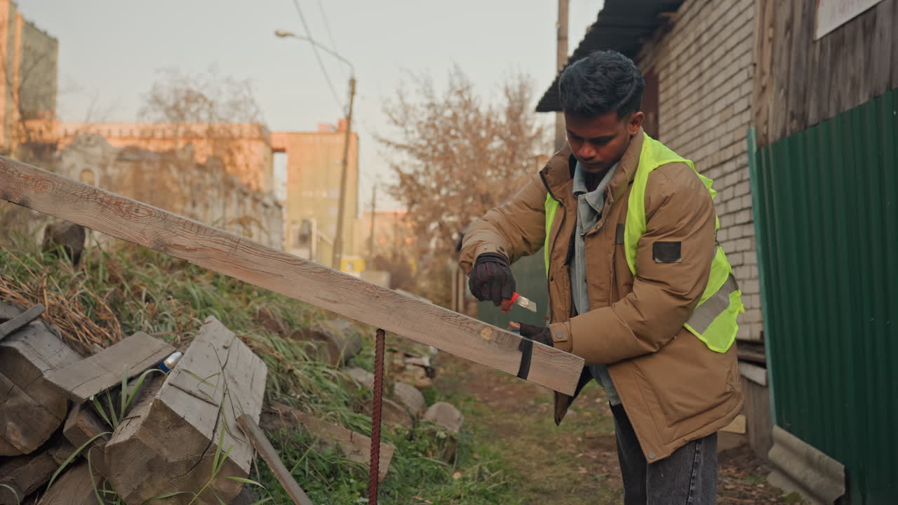 Technicien de maintenance terminant la réparation d'un garde-corps à l'aide d'une perceuse, serrant les dernières vis et vérifiant l'alignement, effectuant un contrôle qualité minutieux dans un cadre extérieur de jardin, portant un gilet réfléchissant, sous une lueur automnale, finalisant l'intervention.