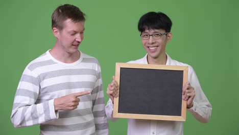 두 명의 행복한 젊은 다민족 사업가들이 검은판을 보여주고 엄지손가락을 올리고 있습니다.