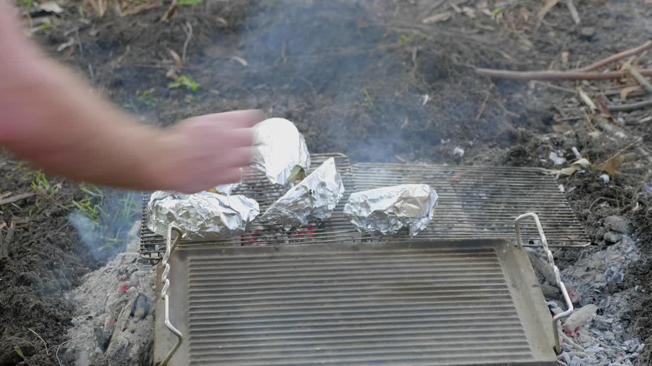 호일로 싸인 야채가 야외 요리 불에 쟁반에 놓여 있습니다.