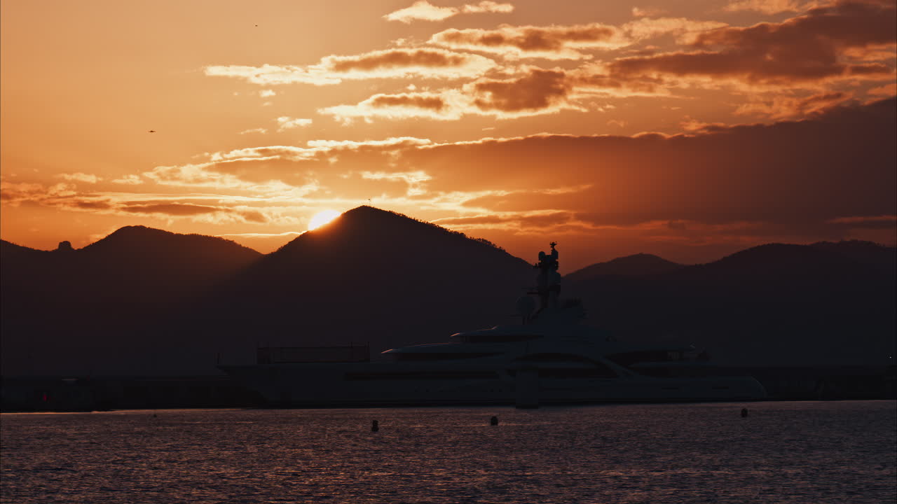 Distant view of a yacht docked on the sea with a mountain on the background at sunset
