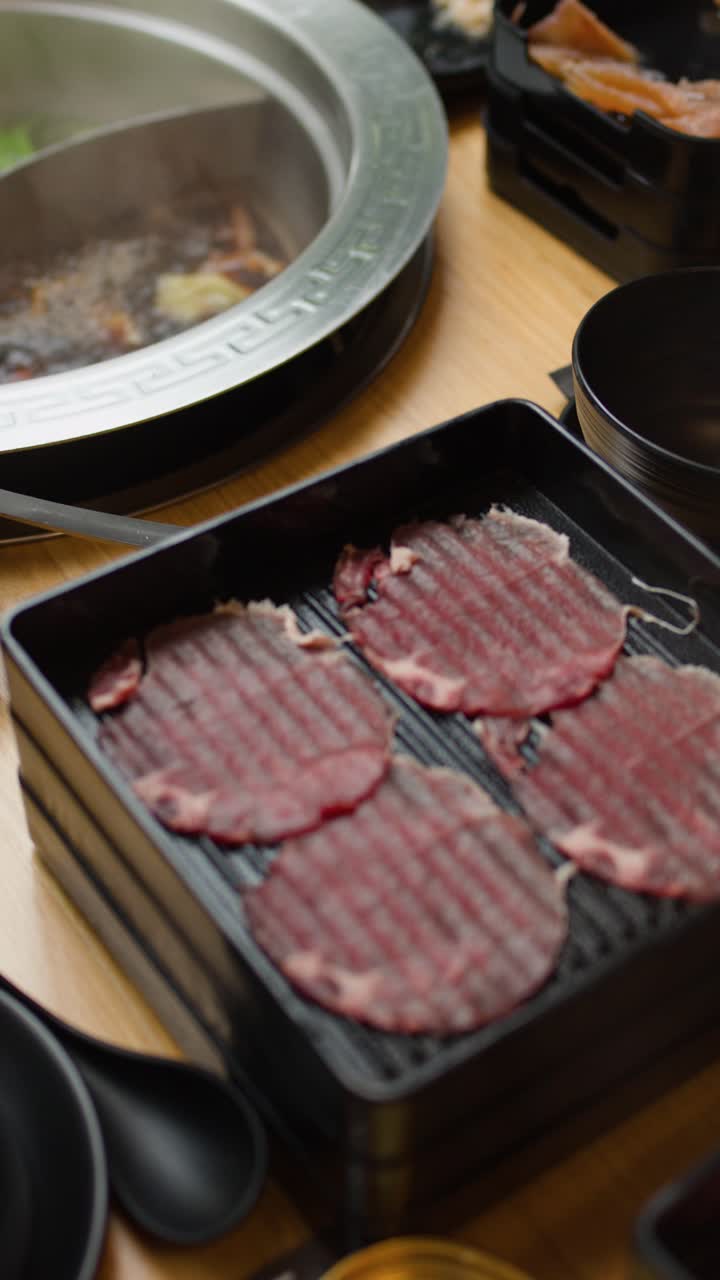 Panci hotpot dua sekat mendidih dengan sayuran dan daging, makan di meja, pencahayaan terang, tampilan kamera dari atas.