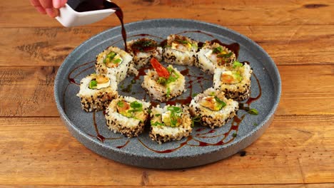 Close-up-of-plate-of-sushi-being-doused-in-eel-sauce-in-a-restaurant