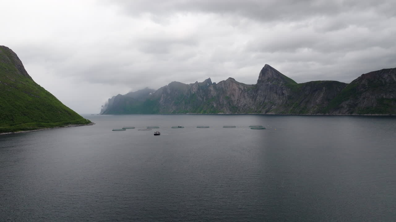 Bredt luftfoto med drone af et lakseopdræt i Mefjord, Senja. De dramatiske, tågede bjerge skaber en stemningsfuld baggrund. Ideelt til akvakultur, industri og episke norske rejsekoncepter
