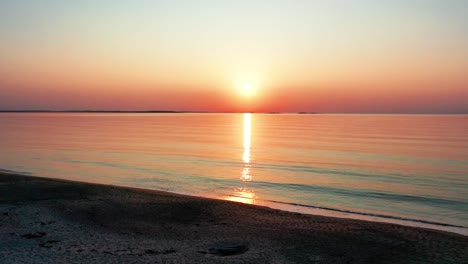 view of ocean sunset while waling on beach with bright glowing sun casting colorful red, orange, purple, and yellow reflections over peaceful rippling waves of the sea with beautiful sky