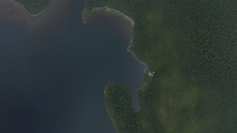 aerial view from the clouds looking down on an isolated cabin in the woods on a lake