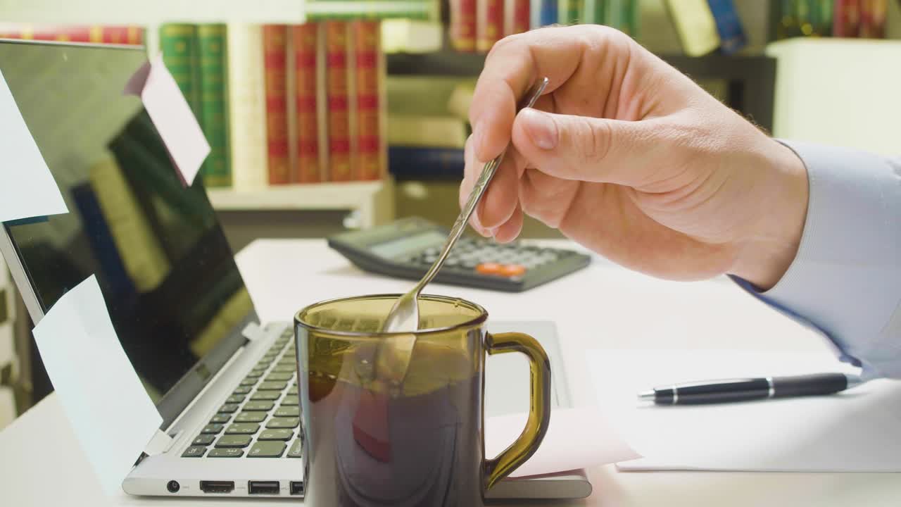 mano masculina agita el azúcar en el café en el lugar de trabajo en la oficina