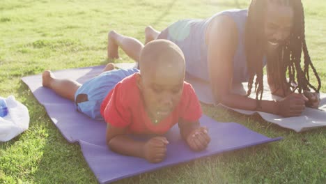 video of happy african american son and father doing plank on grass and doing high five