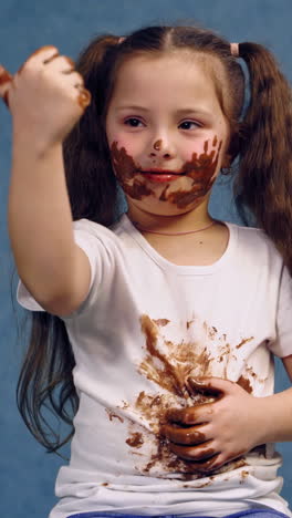 portrait of dirty little girl after eating chocolate. funny child with two ponytails have smeared face and white t-shirt in chocolate. vertical video